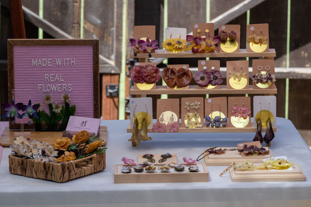 Display of floral earrings on a table with a 'Made with Real Flowers' sign.